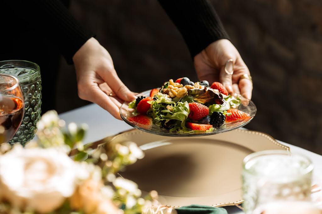 Someone placing a salad plate on a gold charger
